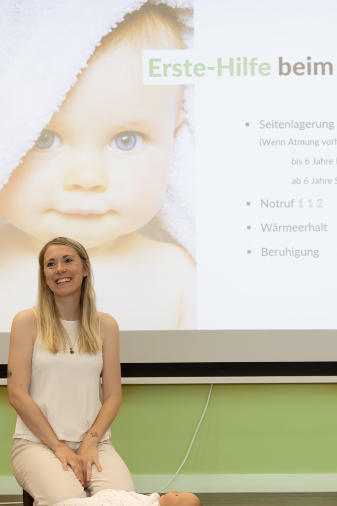 Miriam im Kursraum, im Hintergrund eine Folie zur Ersten Hilfe beim Baby